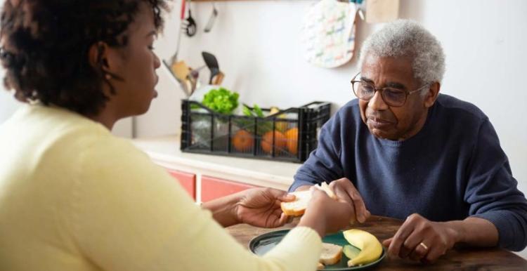 A woman helping an older man eat a meal at a table.