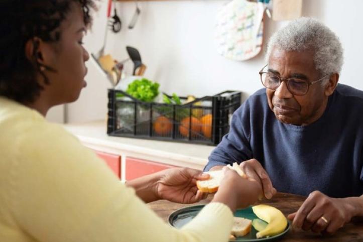 A woman helping an older man eat a meal at a table.