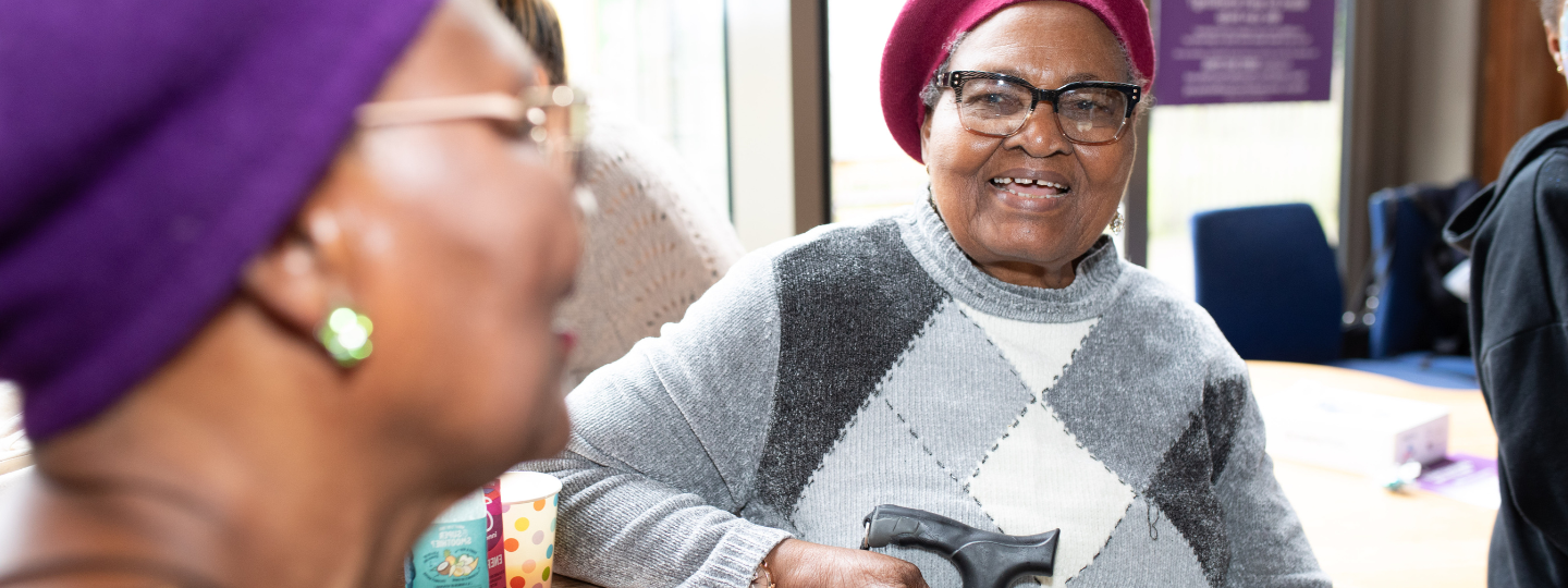 Two older black woman talking and smiling. Both are wearing berets and holding walking sticks.